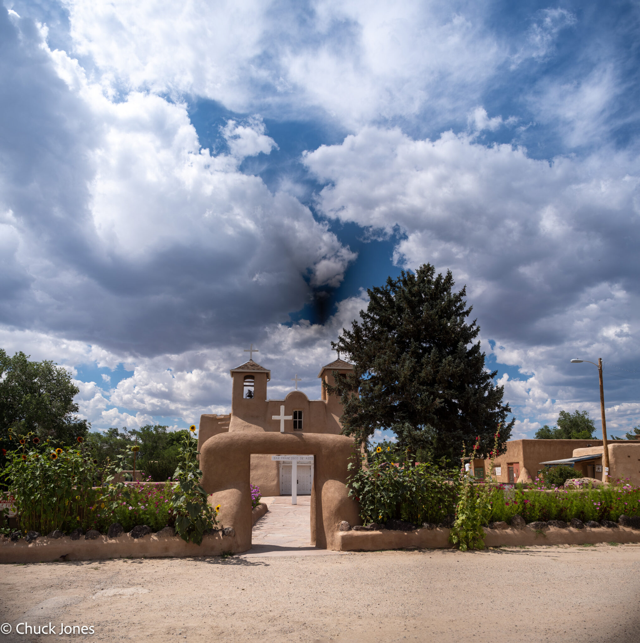 Wider composition stitch showing the entrance gate framing the church