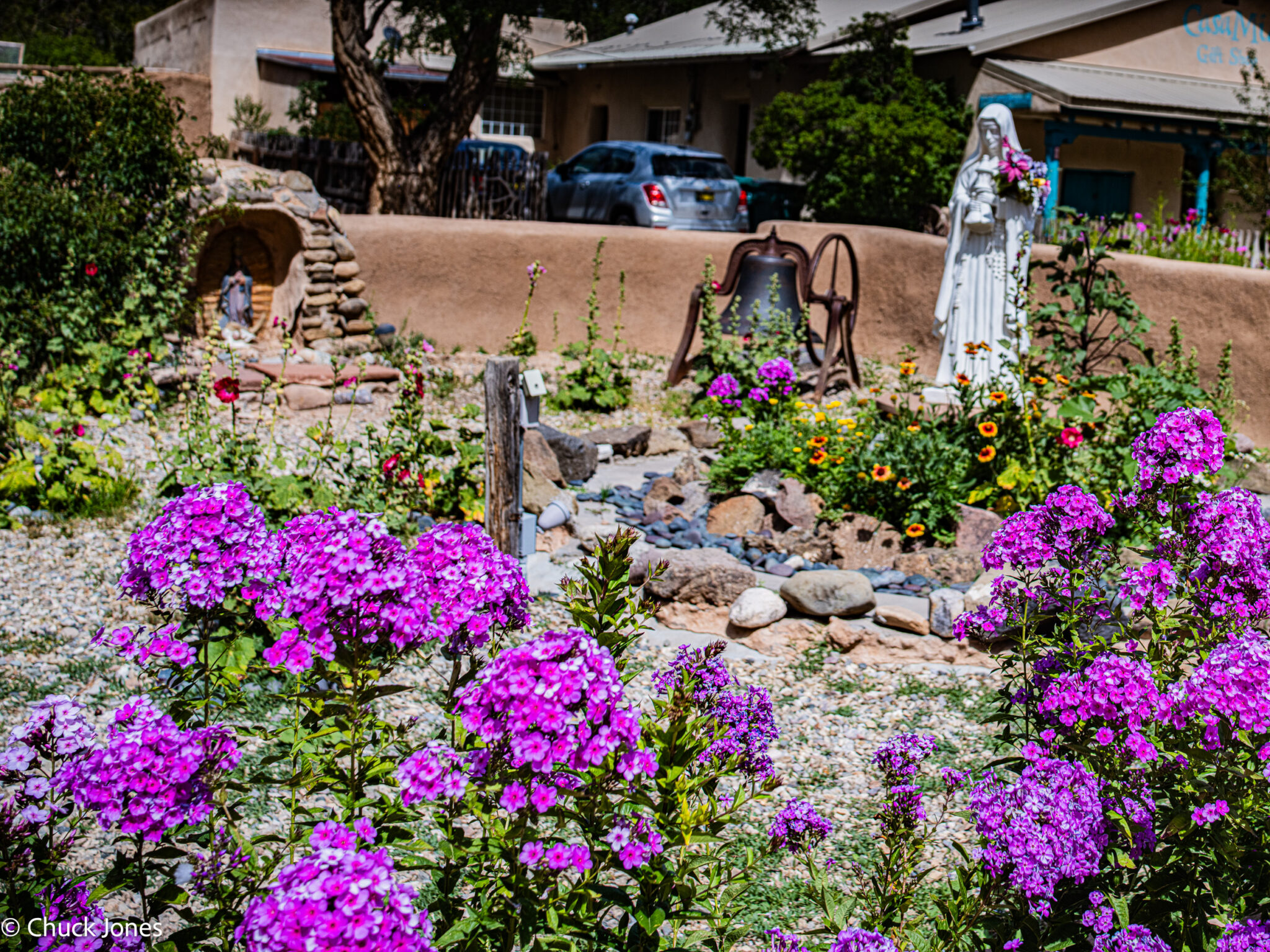 Garden scene with religious statuary, hollyhocks, and phlox in selective focus